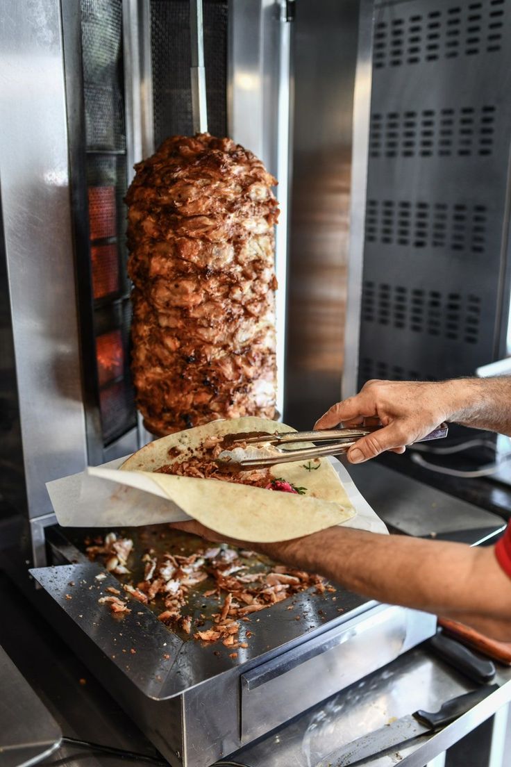 Cuisinier tranchant la viande de la broche de kebab dans une galette