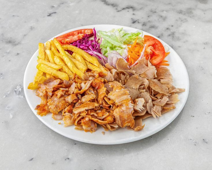 Assiette blanche garnie de viande de kebab, frites, salade et tomates